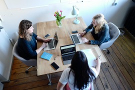 Tre kvinnor som sitter och jobbar med sina datorer runt ett rektangulärt bord.